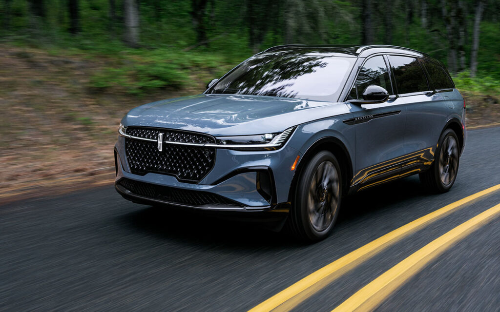 Blue SUV driving on a forest road, showcasing sleek design and glossy finish.