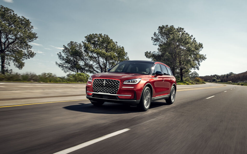 Red SUV driving on a scenic highway with trees and clear sky, showcasing sleek design.