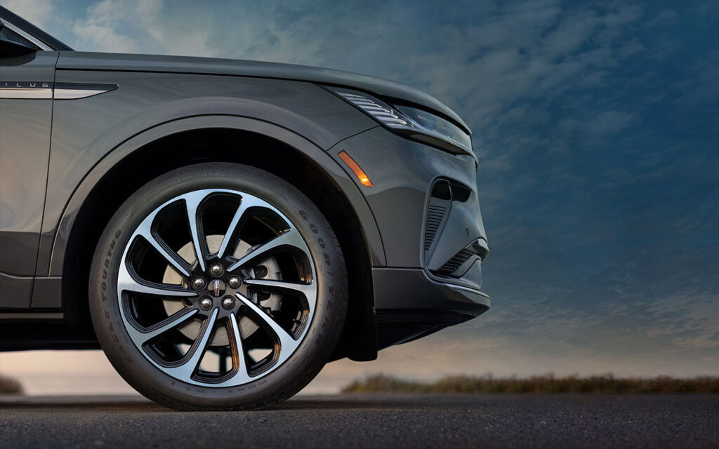 Close-up of a car's front wheel and bumper against a cloudy sky background.